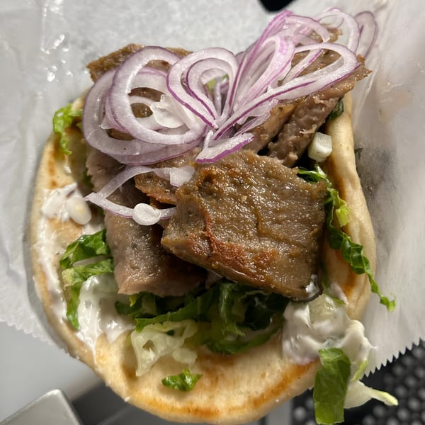 A close-up of a Greek gyro with meat, red onions, lettuce, and tzatziki sauce on pita bread.
