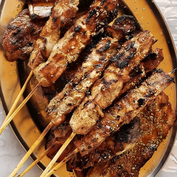 Grilled Greek souvlaki skewers and meat, seasoned with herbs, served on a golden platter.